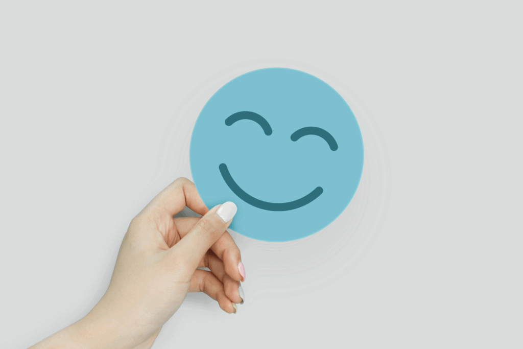 Ein lächelndes Emoji auf einer blauen Karte, gehalten von einer Hand